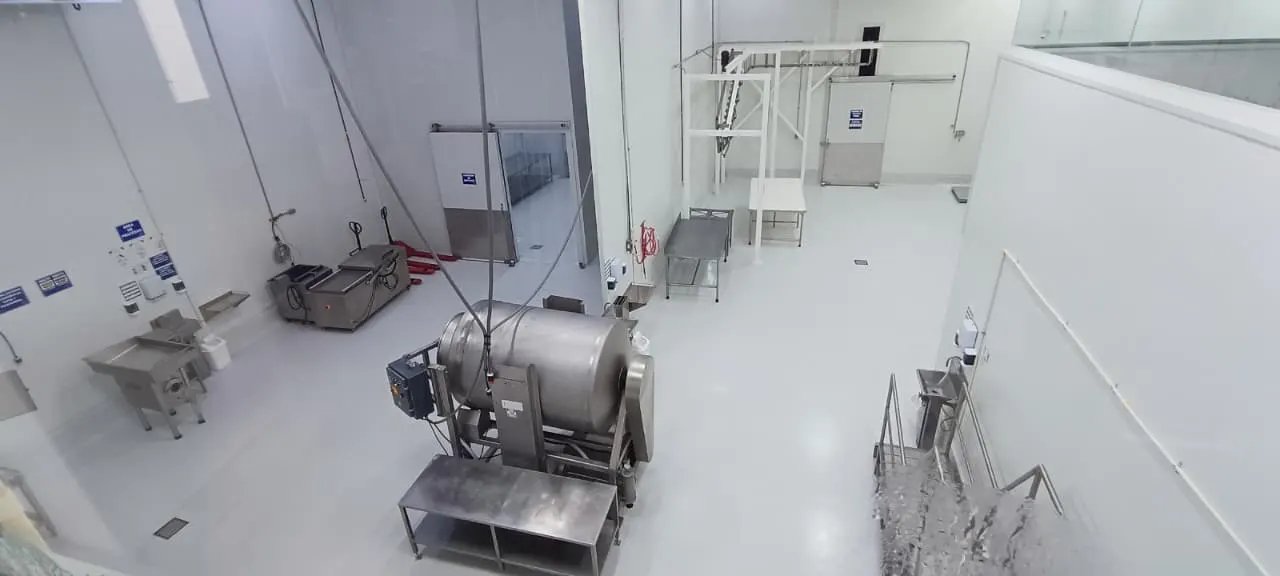 Área de proceso de la planta con masajeador de carne, molino y mesas de acero inoxidable.